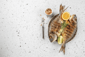 Dwie pieczone ryby z plasterkami cytryny, limonki i rozmarynem, obok miseczka soli i widelec